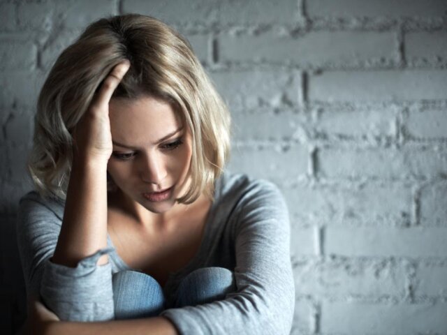 depressed-woman-sitting-against-wall-and-holding-head-in-hand