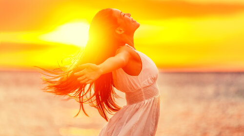 Happy woman feeling free with open arms in sunshine at beach sunset. Freedom and carefree enjoyment 