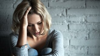 depressed-woman-sitting-against-wall-and-holding-head-in-hand