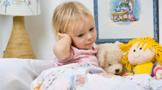 little girl in bed touching ear