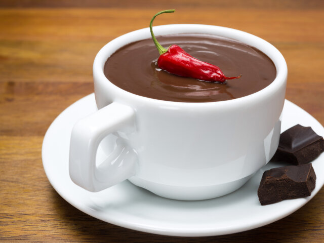 cup of hot chocolate with chili peppers on a wooden background,