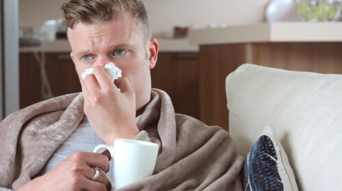 man-with-runny-nose-drinking-hot-drink-at-home-under-blanket-on-sofa
