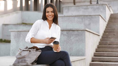 Happy business woman sitting outdoors with cup of coffee