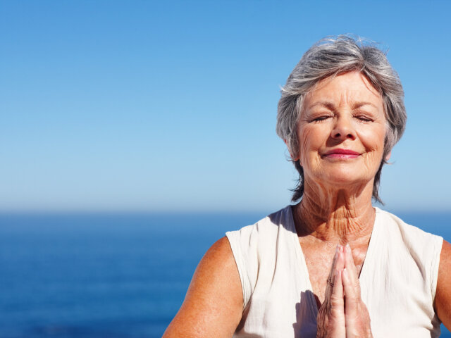 Elderly woman meditating with ocean in the background