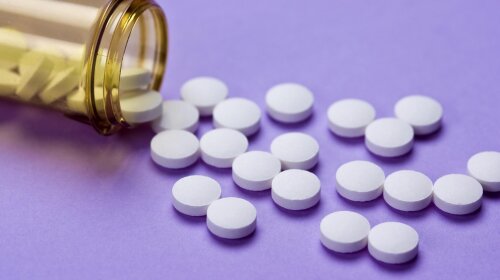 30 generic aspirin tablets scattered from a prescription bottle on a purple surface — ibxars00