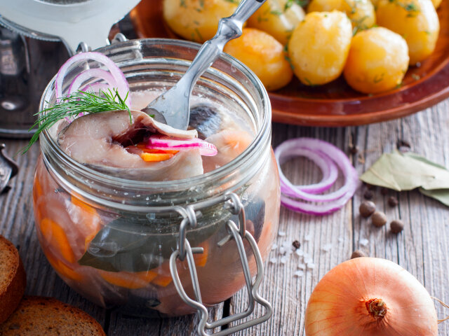 Swedish traditional marinated herring with onions and carrots in a glass jar, selective focus
