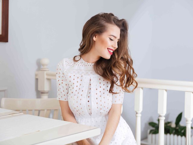 Happy lovely young woman in white dress sitting at cafe