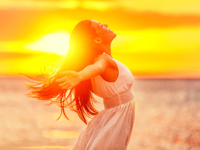 Happy woman feeling free with open in arms sunshine beach at sunset. Freedom and carefree enjoyment 